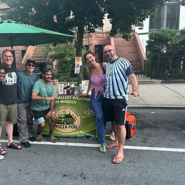 Guests posing with the crew beside the Pod's banner on a brownstone street