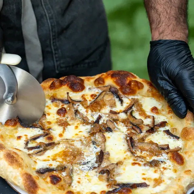 A gloved hand holding a mushroom white pie steady while a wheel cuts it