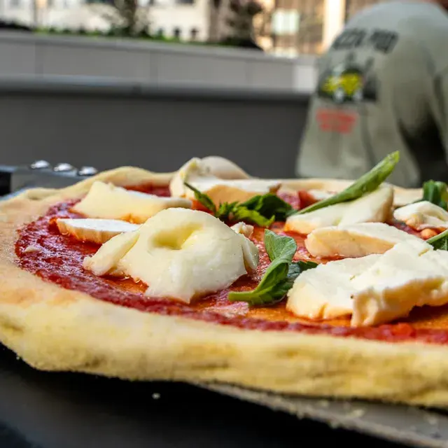 A margherita topped with torn fresh mozzarella and basil, a cook in a Pizza Pod shirt behind it