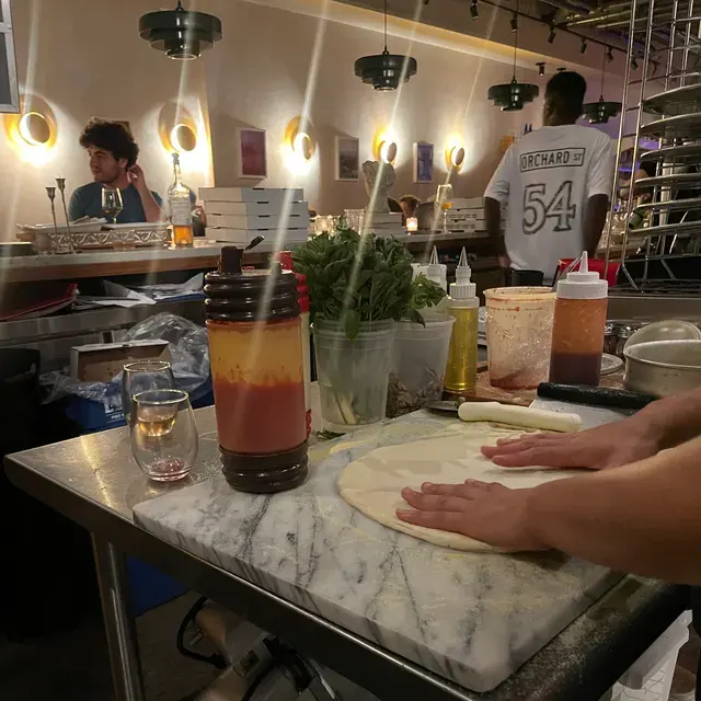 Dough being pressed out on a marble slab, a guest with a glass of wine at the counter behind
