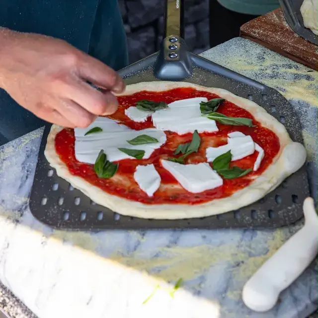 A margherita being finished by hand on a marble counter
