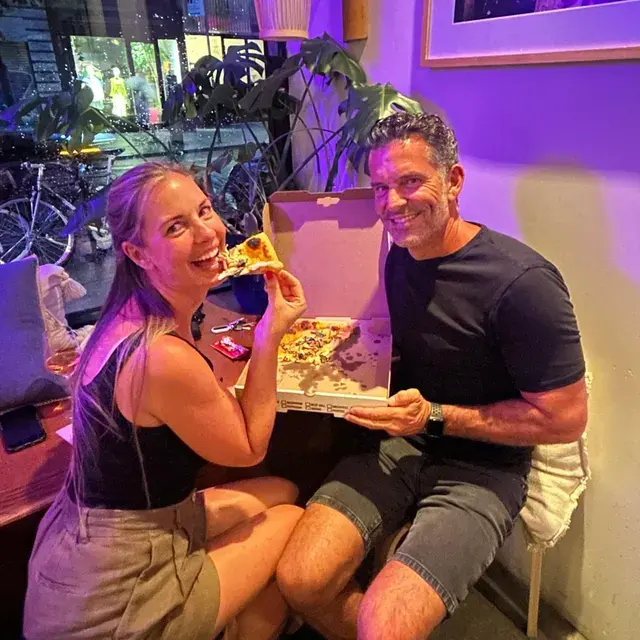 A couple sharing a whole pie on a sofa under purple light