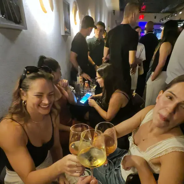 Three guests raising their glasses together at a party, a crowd behind them