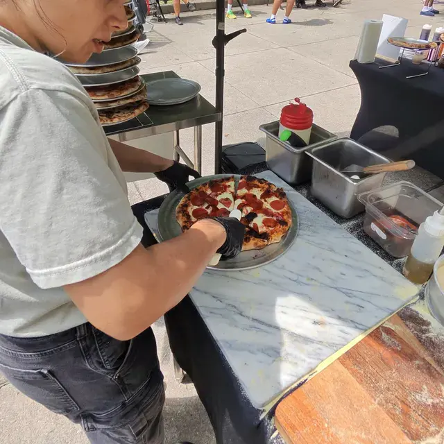 A cook cutting a pepperoni pie on a marble counter at a curbside setup