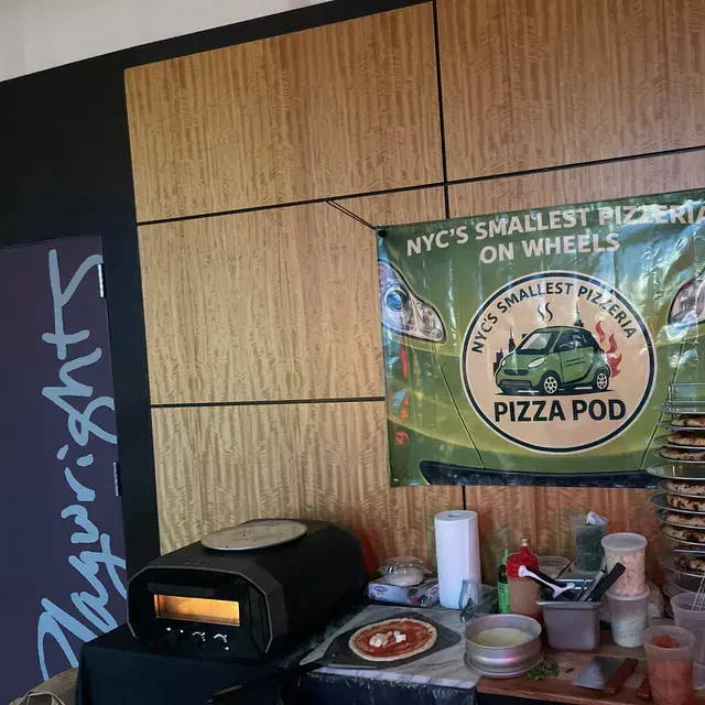 The Pizza Pod banner on a wood-panelled wall above the oven, prep and a rack of pies laid out underneath