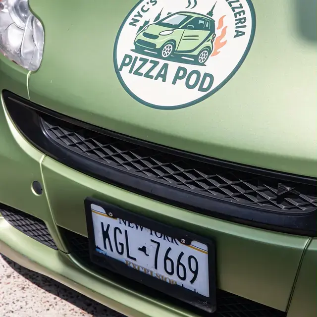 The Pizza Pod badge on the nose of the green Smart Car