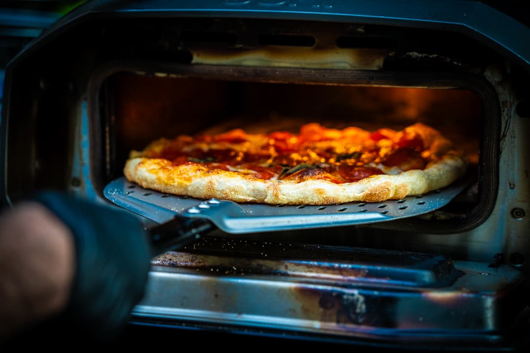 A pepperoni pizza coming out of the electric oven on a perforated peel.